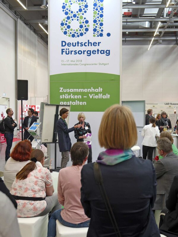 Vortrag am Stand des Deutschen Vereins auf einer Konferenz mit Publikum und einem großen Banner im Hintergrund. – 